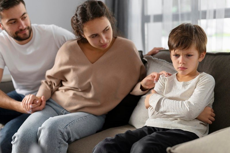 Parents sitting on a couch, consoling a young boy who looks upset, symbolizing family issues or emotional distress.